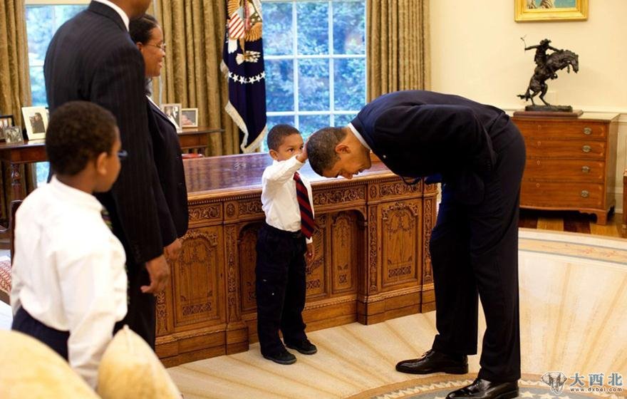 2009年3月8日，一名临时工作人员结束在白宫的工作，来到总统办公室与奥巴马合影告别。总统应工作人员小儿子的要求，低下头让他摸摸自己的头发，看看和自己头型一样不一样。